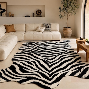 May include: A large, irregularly shaped area rug featuring a high-contrast black and white zebra stripe pattern. The rug has a soft, textured surface and follows the organic, flowing contours of a natural hide shape, covering the floor space.