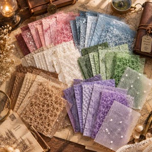 May include: A collection of rectangular paper sheets in various colors including pink, blue, green, purple, and beige. The sheets feature diverse textures, including mesh overlays, embossed patterns, and speckled finishes, arranged in a layered fan.