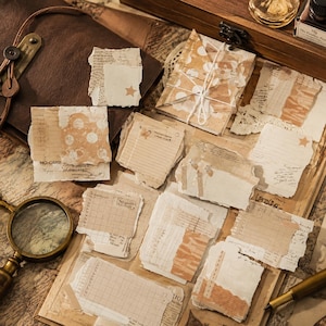 Pode incluir: Uma coleção de pedaços de papel e cartões de papelaria de estilo vintage em tons de bege, creme e castanho. As peças apresentam várias texturas, bordas rasgadas, padrões de grelha, escrita à mão e pequenos motivos de estrelas.