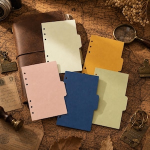 May include: A set of five rectangular paper dividers in cream, yellow, pink, blue, and light green. Each divider features a side tab and a vertical row of six punched holes along the left edge, designed for insertion into a ring-bound notebook system.