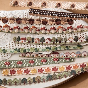 Pode incluir: Uma cole&ccedil;&atilde;o de fitas decorativas de croch&ecirc; com v&aacute;rios padr&otilde;es, incluindo bolotas castanhas, cogumelos vermelhos e brancos, pequenas casas com &aacute;rvores, folhas de trevo verdes, folhas de outono em amarelo e laranja e filas de &aacute;rvores.