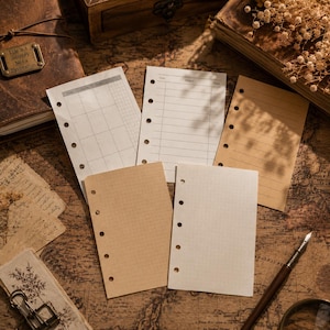 May include: A collection of five loose-leaf planner inserts with six pre-punched holes along the side. The set includes white and kraft paper sheets featuring various layouts such as a monthly grid, lined, grid, and dot grid patterns.