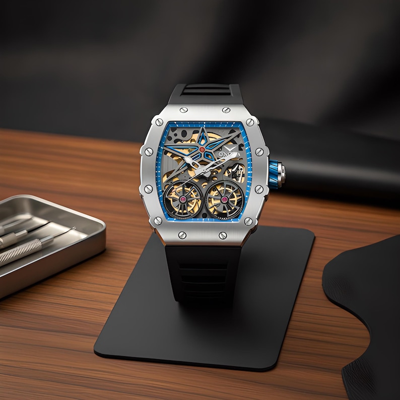 May include: A silver-toned tonneau-shaped wristwatch featuring a skeletonized dial with a prominent blue star motif, dual exposed balance wheels, and a black rubber strap. The watch case is secured with eight visible screws and includes a blue crown.