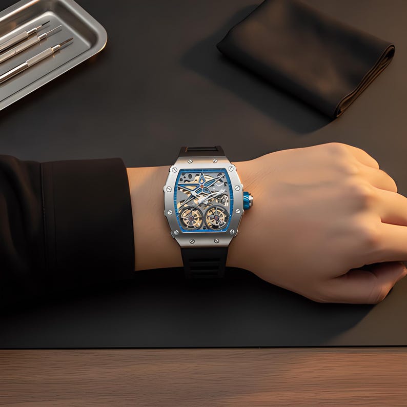 May include: A silver-toned tonneau-shaped wristwatch with a skeletonized dial featuring a prominent blue star-shaped element and visible mechanical gears. The watch has a black rubber strap, a blue crown, and a metallic bezel secured with screws.
