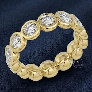 May include: A yellow gold eternity band featuring a series of round, brilliant-cut clear stones set in individual bezel settings. The ring displays a continuous circular design with polished metal edges surrounding each stone, creating a uniform look.