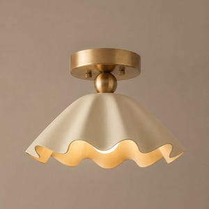 May include: A flush mount ceiling light fixture featuring a matte cream-colored, scalloped-edge shade. The fixture is attached to a circular, brushed brass-toned metal canopy with a central spherical connector piece, creating a cohesive design.