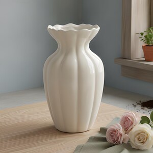 May include: A white ceramic vase with a scalloped rim and vertical ribbed detailing along the body. The vase has a rounded, bulbous shape that tapers toward the neck and flares out at the top, featuring a smooth, glossy finish throughout.