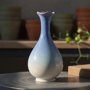 May include: A ceramic vase with a narrow neck and a bulbous base, featuring a gradient color transition from a soft white at the bottom to a light blue at the top. The surface has a fine crackle glaze finish and a scalloped, wavy rim opening.