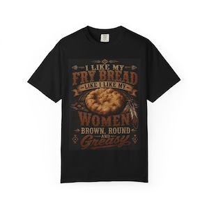 May include: A black short-sleeved t-shirt featuring a graphic print of a piece of fry bread. The text reads: I LIKE MY FRY BREAD LIKE I LIKE MY WOMEN BROWN, ROUND AND GREASY. The design includes decorative feather and geometric patterns in brown tones.