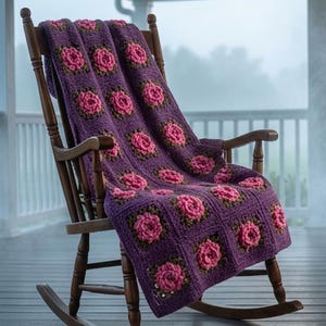 May include: A handmade crochet blanket featuring a repeating pattern of purple squares with central pink floral motifs and dark green accents. The blanket is draped over a wooden rocking chair with a high back, curved armrests, and two rockers.