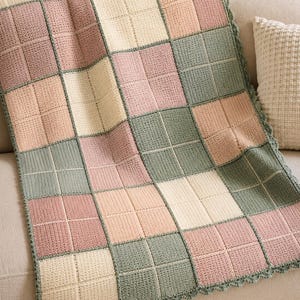 May include: A handmade crochet blanket featuring a grid pattern of alternating square blocks in muted shades of sage green, dusty rose, and cream. The blanket is finished with a scalloped edge border in sage green, showcasing a textured stitch.
