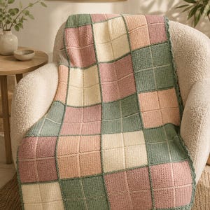 Pu&ograve; includere: Una coperta all'uncinetto caratterizzata da un motivo a griglia di quadrati alternati in tonalit&agrave; verde salvia tenue, crema delicato e rosa antico. La coperta presenta un bordo smerlato ed &egrave; composta da quadrati uniti in un motivo a scacchiera.