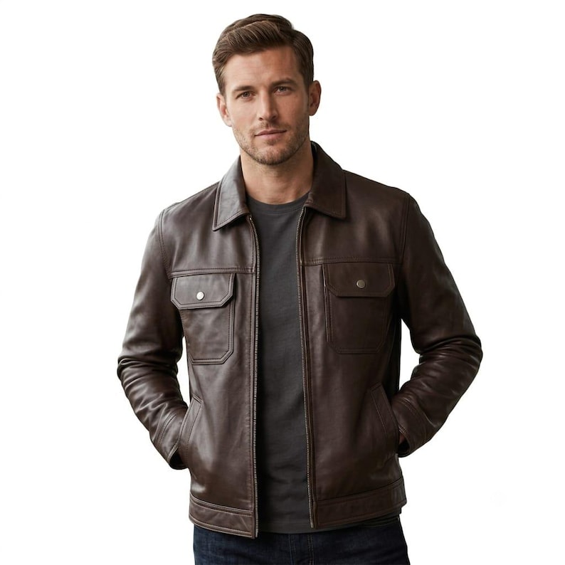 Puede incluir: Una chaqueta de cuero marr&oacute;n oscuro con cuello cl&aacute;sico, cremallera frontal completa y dos bolsillos en el pecho con solapas abotonadas. La chaqueta se lleva sobre una camiseta gris oscuro lisa, mostrando un corte estructurado.