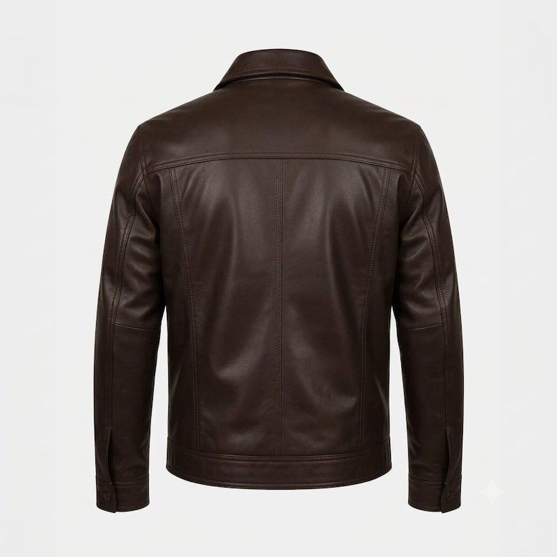 Puede incluir: Una chaqueta de cuero marr&oacute;n oscuro vista desde atr&aacute;s, con un cuello cl&aacute;sico doblado, mangas largas con pu&ntilde;os abotonados, un canes&uacute; horizontal en la espalda y detalles de costuras verticales que bajan por el centro del panel trasero hasta el dobladillo.