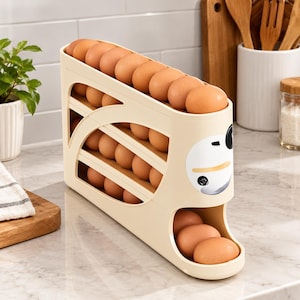 May include: A cream-colored plastic egg dispenser rack with a tiered gravity-fed design. The unit holds multiple brown eggs in rows, featuring a rounded front end with a stylized black and white graphic print and a bottom opening for egg retrieval.