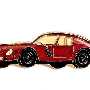 Puede incluir: Un pin de solapa de esmalte rojo con forma de coche deportivo vintage con bordes de metal dorado. El coche presenta un capó largo, un parabrisas y ventanas laterales de color crema, ruedas negras y distintivas rejillas de ventilación laterales.