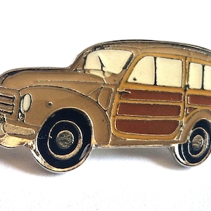 Puede incluir: Un pin de esmalte metálico con forma de coche familiar antiguo. El vehículo presenta una carrocería de color tostado, paneles laterales de madera marrón oscuro, ventanas de color crema y ruedas negras con centros plateados. Borde de metal plateado.