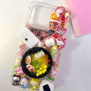 May include: A clear phone case decorated with various miniature charms including a bowl of ramen, Hello Kitty figures, a white quilted handbag, a bag of potato chips, a carton of milk, and an onigiri rice ball, all arranged on the back surface.