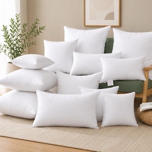 Puede incluir: Una colección de varios rellenos de cojín blancos en formas cuadradas y rectangulares. Los cojines son lisos, suaves y están rellenos, con un exterior de tela blanca limpia. Están dispuestos en una exhibición apilada y en capas, mostrando diferentes tamaños y orientaciones para un uso versátil en la decoración del hogar.