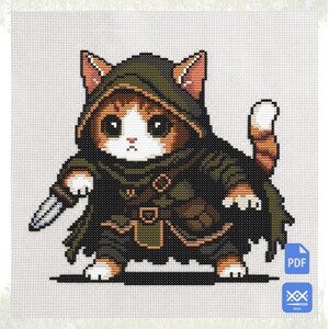 May include: A cross-stitch pattern featuring a ginger and white cat wearing a dark green hooded cloak and belt, holding a small silver dagger. The cat has large black eyes and a white face. A blue PDF icon and a blue SAGA icon are in the corner.
