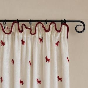 May include: An off-white curtain featuring a repeating pattern of small red horse silhouettes. The top edge has a ruffled header trimmed with a dark red fabric border, and the curtain hangs from a black metal rod with circular rings.