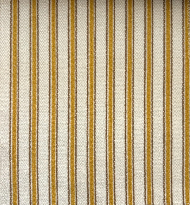 May include: A woven fabric featuring a repeating pattern of vertical stripes in mustard yellow and brown against an off-white background. The textile displays a distinct herringbone weave texture throughout the entire surface of the material.
