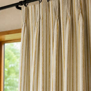 May include: A pinch-pleated curtain panel featuring a vertical striped pattern in shades of mustard yellow, white, and dark gray. The fabric hangs from a black metal curtain rod with matching black circular rings, creating uniform folds.