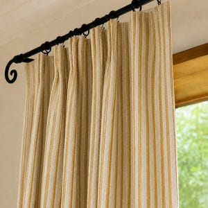 May include: A pleated curtain panel featuring a vertical striped pattern in mustard yellow and off-white. The fabric hangs from a black metal curtain rod with decorative scroll ends, secured by black circular rings that hold the fabric in place.