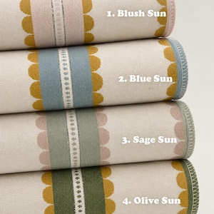 May include: Four rolled fabric textiles featuring a central vertical stripe with scalloped edges in mustard yellow, flanked by a solid color band and a thin decorative center strip. The labels read: 1. Blush Sun, 2. Blue Sun, 3. Sage Sun, 4. Olive Sun.