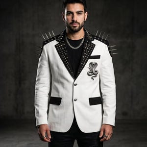 Può includere: Un blazer bianco con revers neri decorati con borchie argentate e lunghe punte metalliche sulle spalle. Il capo presenta un fazzoletto da taschino nero, due bottoni frontali e una toppa ricamata raffigurante un cobra sul petto sinistro.