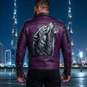 Op de afbeelding: Een paarse leren jas met een grote, gedetailleerde illustratie van een huilende wolf op de rug. De jas is versierd met zilveren metalen spikes op de schouders, mouwen en kraag, en is voorzien van zilverkleurige ritsen bij de mouwboorden.