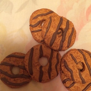 May include: Five round cookies with a brown and dark brown striped pattern. The cookies have a hole in the center.