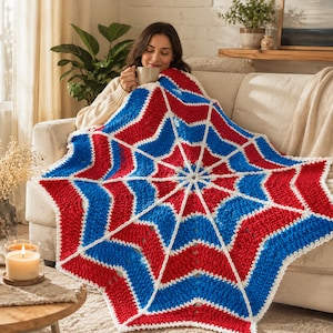Könnte beinhalten: Eine handgefertigte Häkeldecke mit einem lebendigen Sternmuster aus abwechselnden Abschnitten in leuchtendem Rot, Königsblau und Weiß. Das Design strahlt von einem Mittelpunkt aus und erzeugt eine geometrische Optik mit strukturierten Maschen.