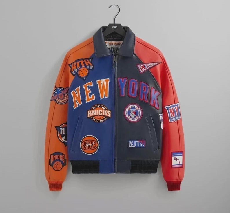 Puede incluir: Una chaqueta universitaria de cuero multicolor con paneles naranjas, azules y azul marino. El frente muestra parches bordados que incluyen el texto NEW YORK, KITH y varios logotipos de baloncesto. Tiene un cuello camisero y pu&ntilde;os acanalados.