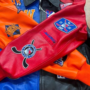 Puede incluir: Una chaqueta universitaria de cuero multicolor con paneles llamativos en rojo, naranja, azul y negro. La chaqueta est&aacute; adornada con varios parches bordados, incluyendo los logotipos de los New York Rangers y los Knicks, junto con la marca Kith y palos de hockey.