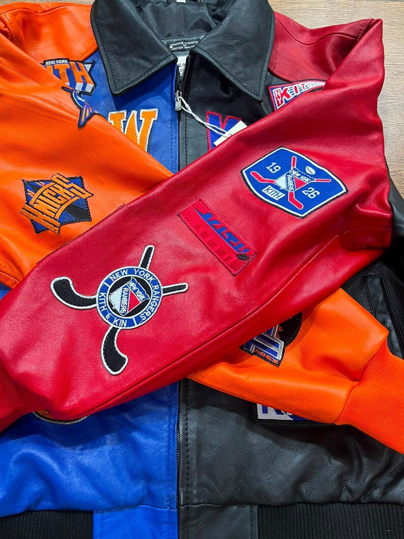 Puede incluir: Una chaqueta universitaria de cuero multicolor con paneles llamativos en rojo, naranja, azul y negro. La chaqueta est&aacute; adornada con varios parches bordados, incluyendo los logotipos de los New York Rangers y los Knicks, junto con la marca Kith y palos de hockey.