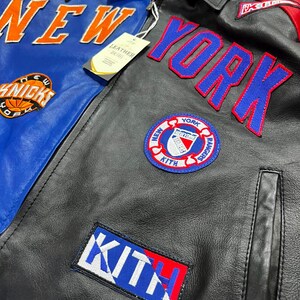 Puede incluir: Una chaqueta de cuero negra y azul con parches y letras bordadas en naranja, azul y blanco. La chaqueta muestra el texto NEW YORK, KITH y KNICKS, junto con un logotipo circular de los New York Rangers y una etiqueta de cuero adjunta.