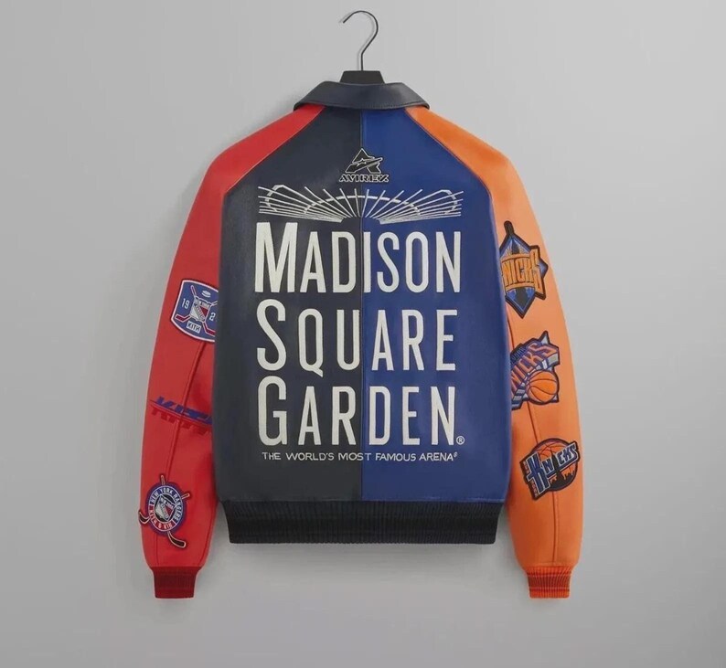 Puede incluir: Una chaqueta universitaria multicolor con un panel trasero azul oscuro con el texto blanco Madison Square Garden The World's Most Famous Arena. Las mangas son rojas y naranjas con varios parches y logotipos de equipos deportivos.