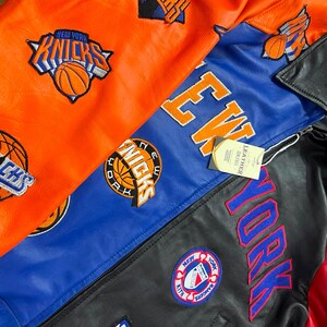 Puede incluir: Una colecci&oacute;n de chaquetas de cuero con paneles vibrantes en naranja, azul y negro. Las chaquetas est&aacute;n adornadas con logotipos bordados del equipo de baloncesto New York Knicks, letras grandes de New York y un parche circular de New York Rangers.