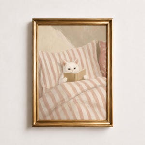 Könnte beinhalten: Ein gerahmter Kunstdruck, der eine weiße Katze im Bett zeigt, die auf einem Kissen und einer Bettdecke mit rosa-weißen Streifen liegt. Die Katze hält ein offenes Buch mit beiden Pfoten. Das Bild befindet sich in einem schlichten Goldrahmen.