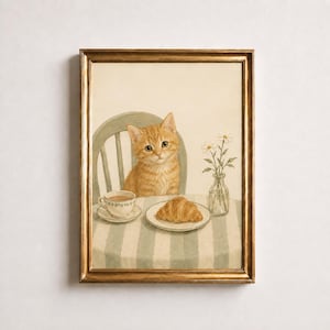 May include: A framed wall art print featuring an orange tabby cat sitting at a table with a striped tablecloth. On the table sits a white teacup on a saucer, a croissant on a small plate, and a clear glass vase containing three white daisies.