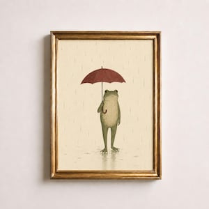 Può includere: Una stampa artistica incorniciata raffigurante una rana verde chiaro in piedi sotto la pioggia mentre tiene un ombrello rosso scuro. L'illustrazione è su uno sfondo color crema con linee verticali che rappresentano le gocce di pioggia.