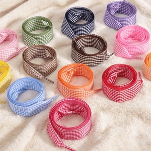 May include: A collection of flat shoelaces arranged in a circular pattern, each featuring a small-scale gingham check pattern. The set includes laces in various colors: green, navy blue, purple, pink, brown, orange, red, light blue, and yellow.