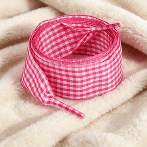 May include: A roll of ribbon featuring a vibrant pink and white gingham check pattern. The ribbon is coiled into a circular shape with one end extending outward, showcasing the consistent woven texture and the classic checkered design throughout.