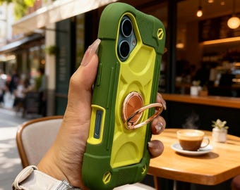 May include: A dual-tone olive green and lime yellow protective phone case featuring a circular rose gold metal ring stand on the back. The case has a rugged, textured design with reinforced corners and precise cutouts for the camera lenses.