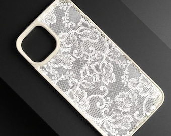 May include: A rectangular phone case featuring a white lace pattern with intricate floral and vine details set against a clear background. The case has a solid white border and a square cutout for a camera lens located in the upper left corner.