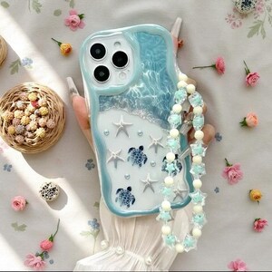 May include: A light blue and white phone case featuring a three-dimensional ocean wave design with embedded starfish, sea turtle figures, and small pearls. The case includes a decorative beaded wrist strap made of translucent star-shaped beads.