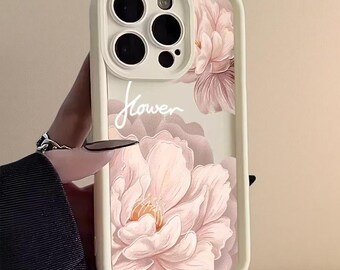 以下が含まれることがあります： クリーム色のスマートフォンケースで、淡いピンク色の大きなピオニーの花柄と、白い筆記体で「flower」という文字がデザインされています。ケースにはカメラ用の盛り上がったフレームと、同系色のクリーム色の保護エッジが付いています。