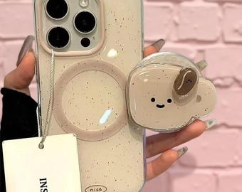 May include: A beige speckled phone case with a circular magnetic ring and a matching beige coffee mug-shaped phone grip featuring a small smiling face. A white rectangular tag with the text INS HOU is attached to the case by a thin cord.