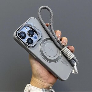 May include: A matte gray smartphone case featuring a circular magnetic charging ring with a lightning bolt icon, a raised camera lens protector labeled CASE.PRO, and a thick, braided gray wrist strap attached to the side with a ribbed connector.